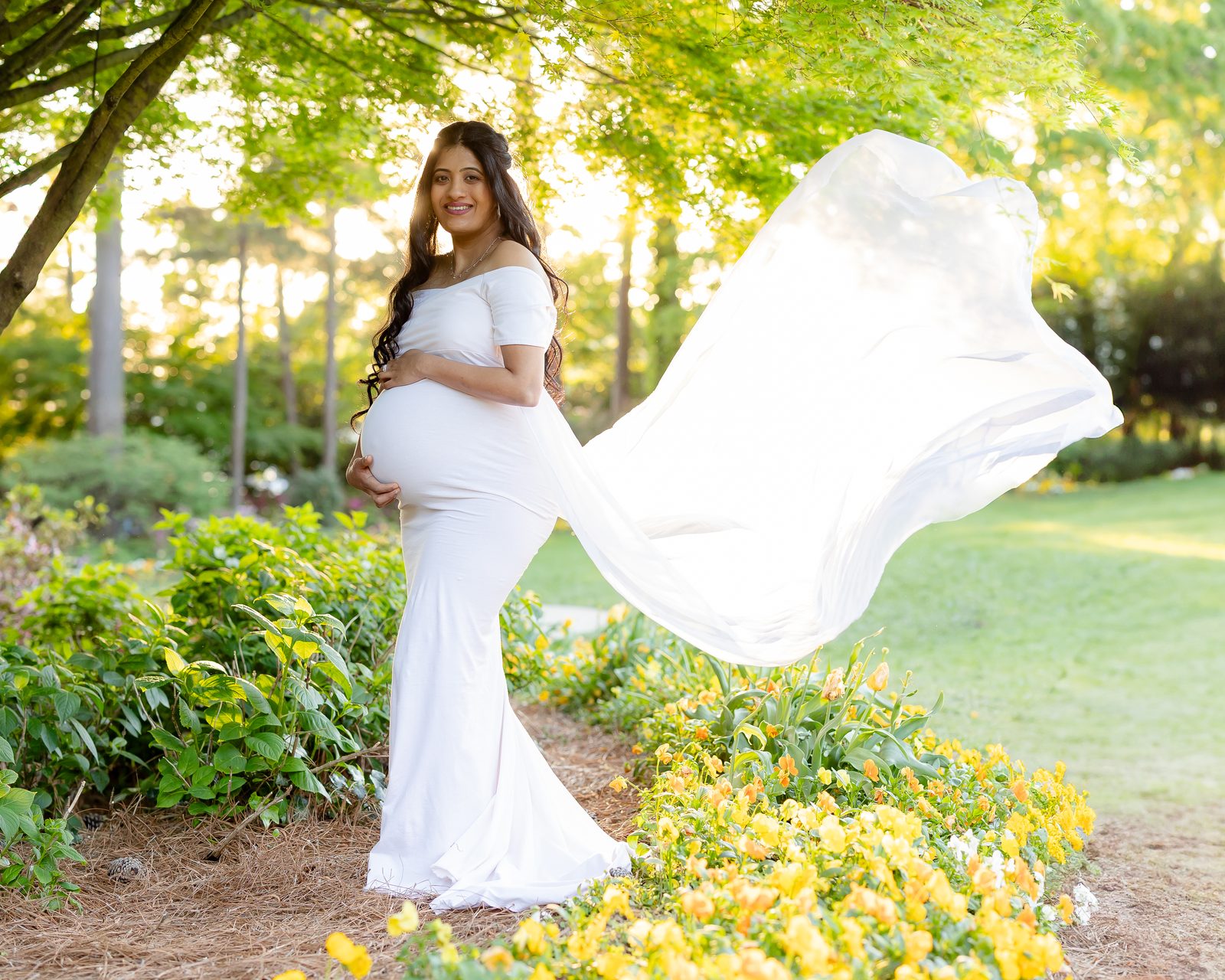 Maternity portrait in white flowing gown in garden