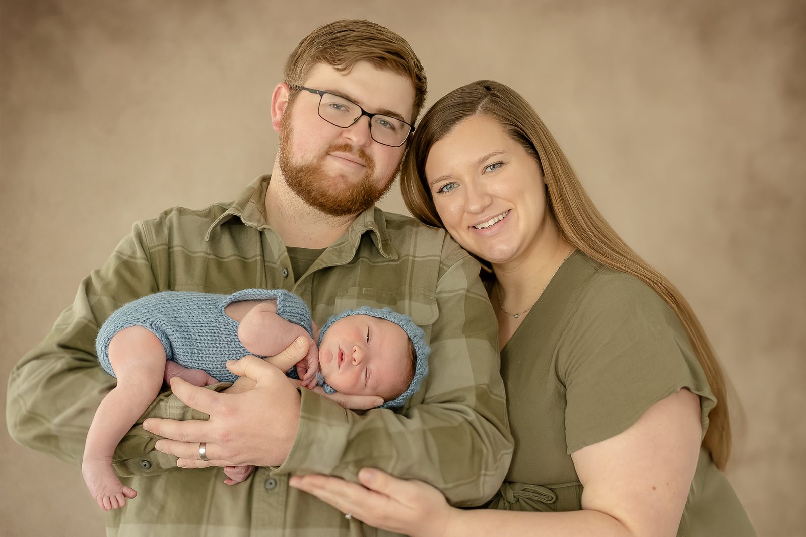 New parents holding their newborn, dressed in a blue knit romper and bonnet