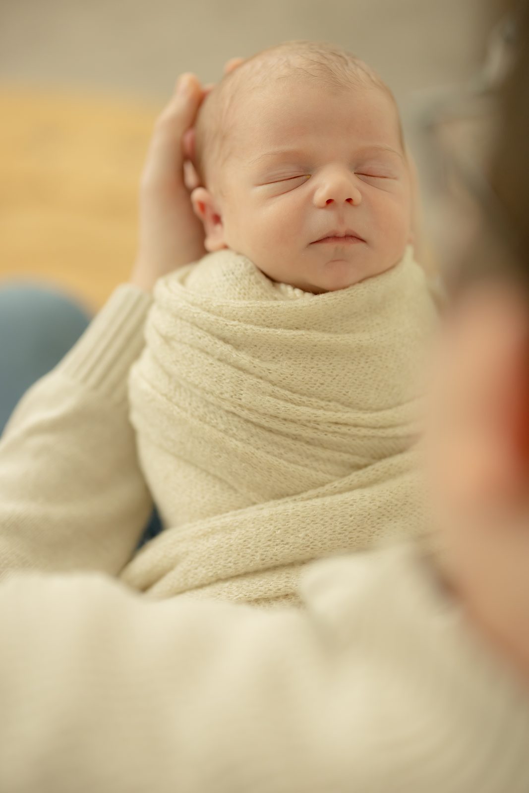 Newborn wrapped in cream, held close and sleeping