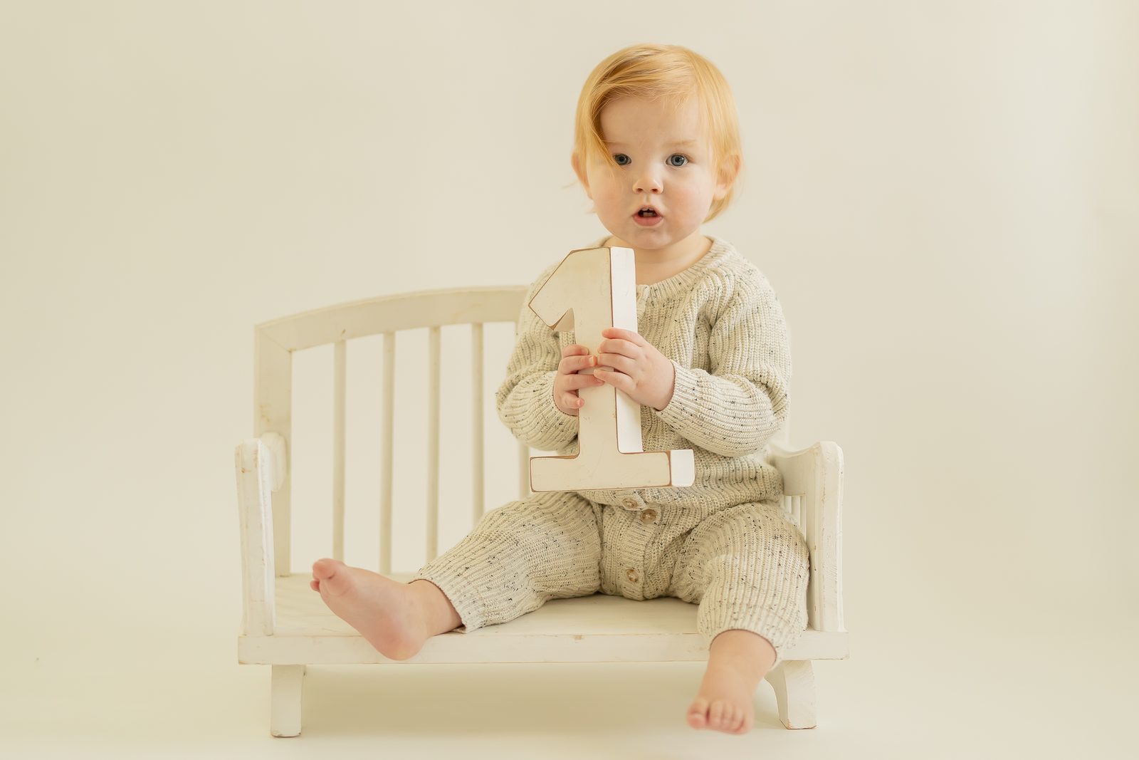 One-year-old in cream knit holding number one