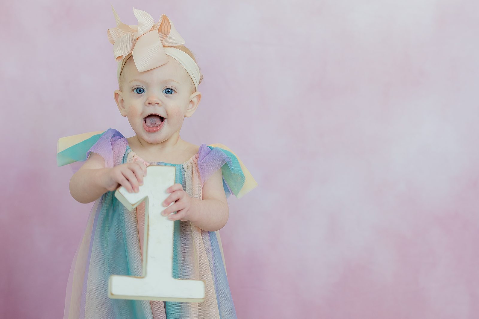 One-year-old in rainbow tulle dress with number one