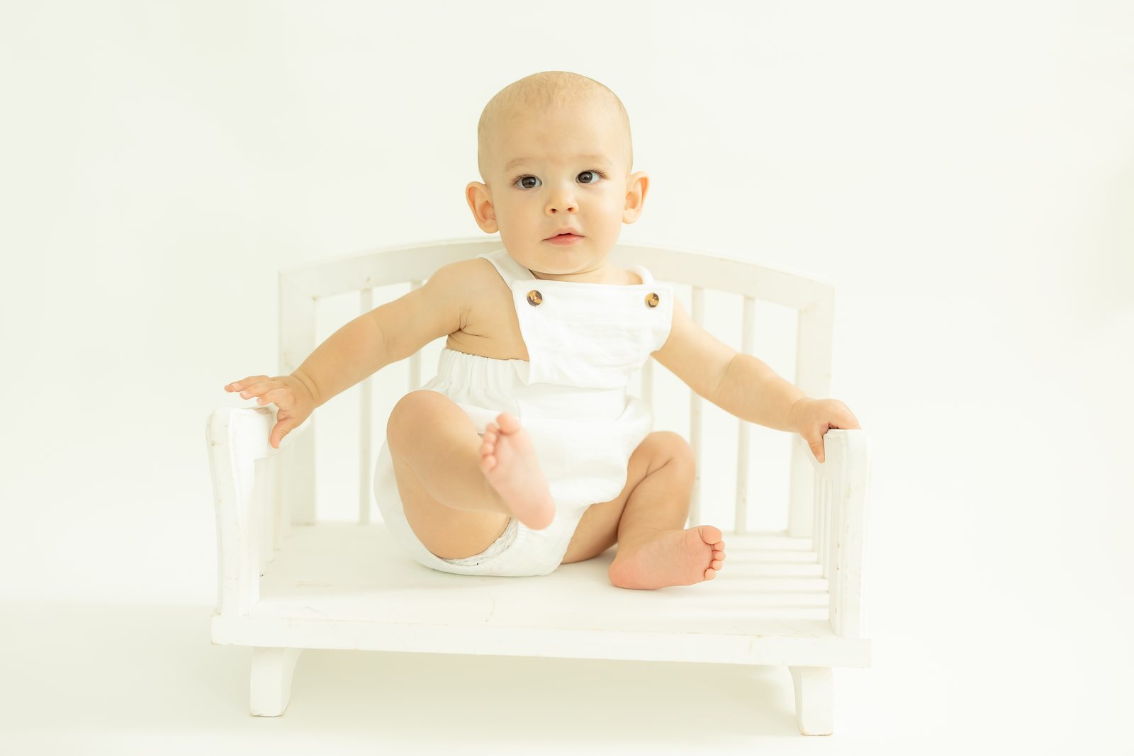One-year-old in white romper on bench