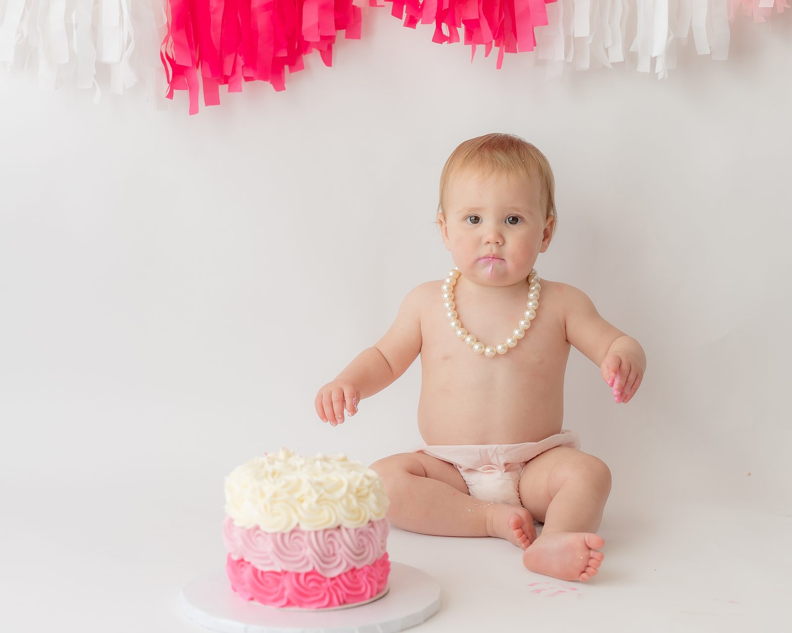 One-year-old with pearls and pink rose cake smash
